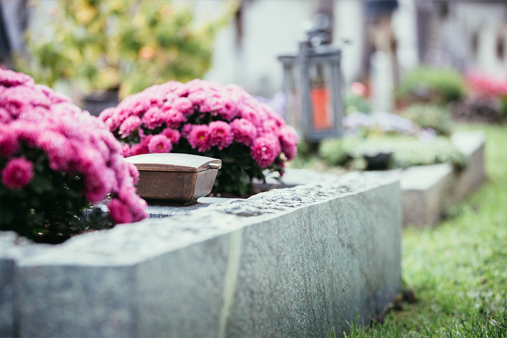 a cemetery with a grave in focus with pink flowers placed around it